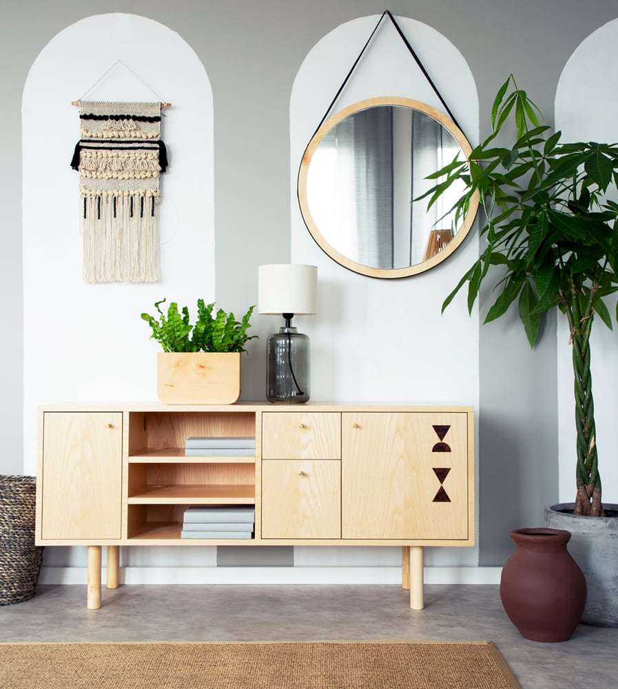 Sala de estar com espelho redondo pendurado sobre aparador de madeira claro