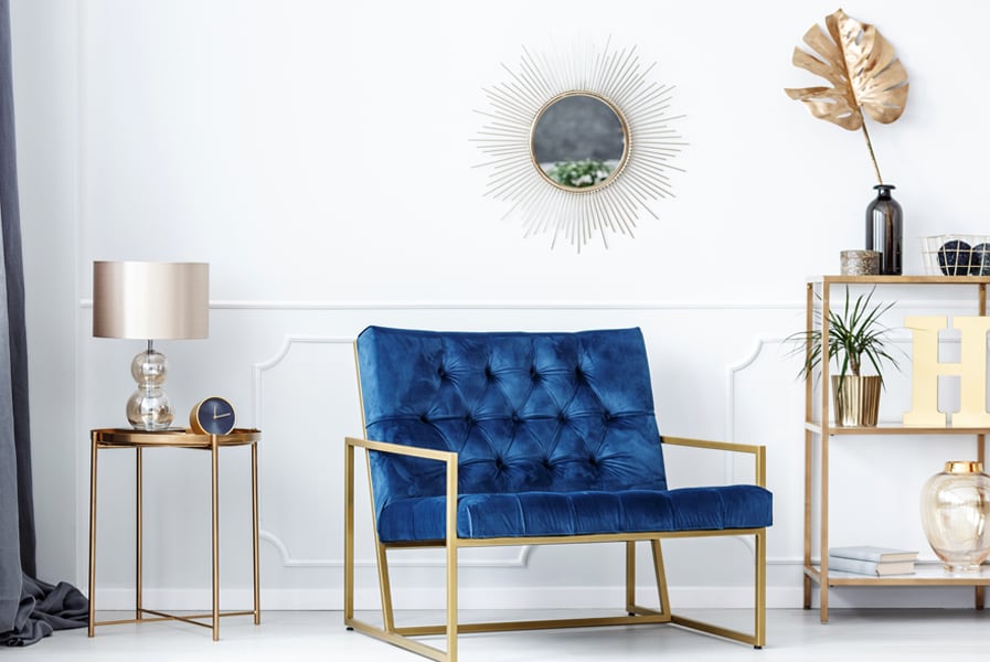 Sala de estar com poltrona de veludo azul e espelho dourado redondo
