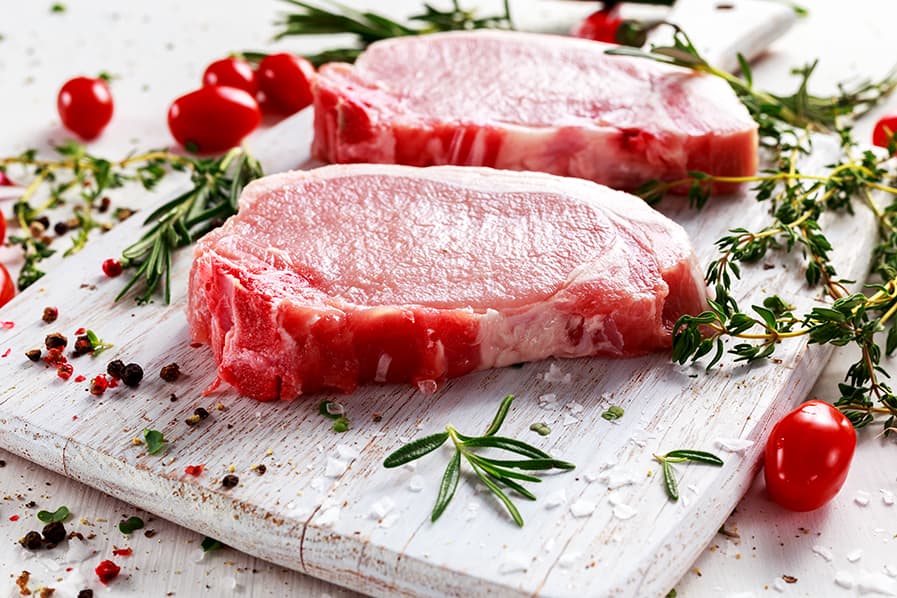 Cortes de carne vermelha ao lado de temperos frescos e tomates cereja