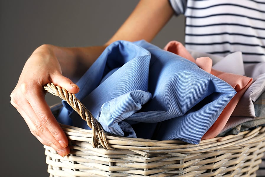 Pessoa segura cesto de vime com roupas para lavagem
