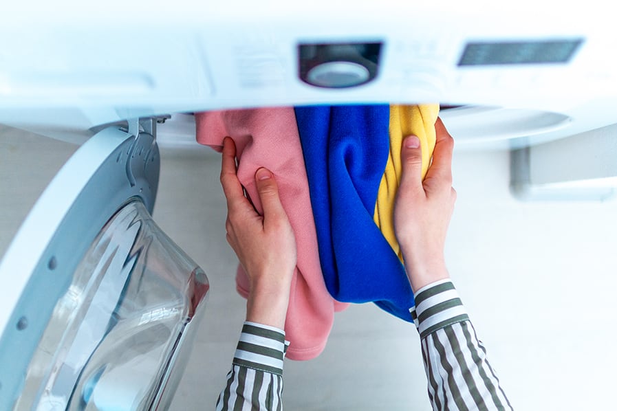 Pessoa retira roupas coloridas da máquina de lavar com abertura frontal