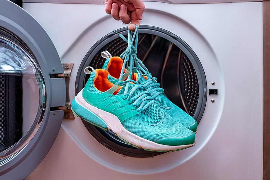 Um par de tênis de corrida da cor azul turquesa sendo colocados dentro da máquina de lavar roupa