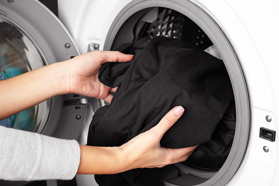 Pessoa retira roupa preta da máquina de lavar