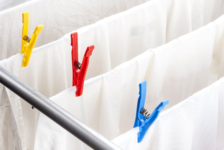 Varal com roupas de cama brancas e pregadores coloridos.