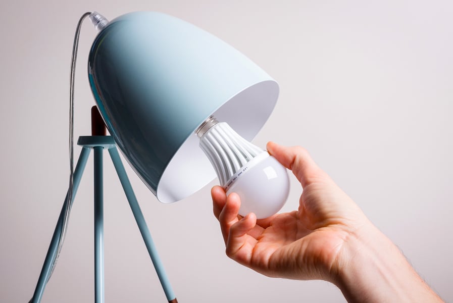 Uma mão troca a lâmpada de um abajur de cor azul clara.