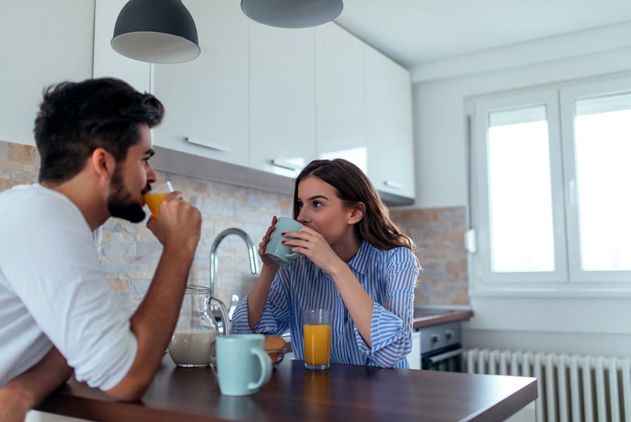 casal toma café da manhã na cozinha de casa com canecas e suco de laranja