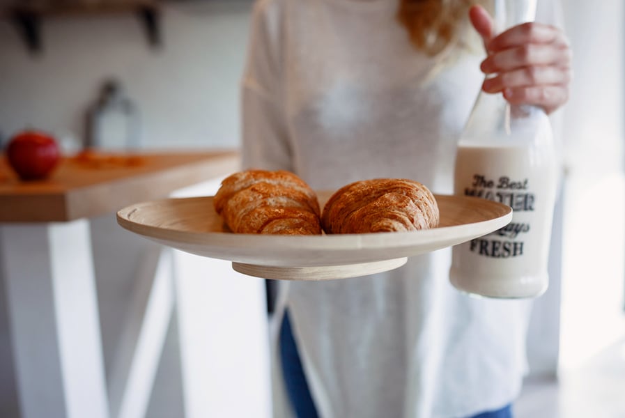 mulher segura um prato na cozinha com croissants e uma garrafa de vidro com leite