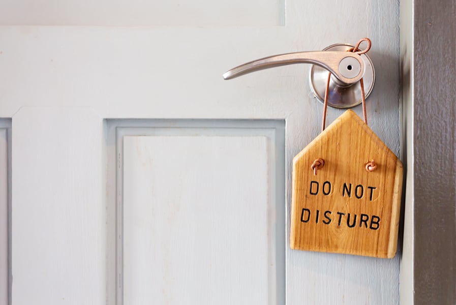 Fechadura da porta com uma placa de madeira que diz “Do Not Disturb”.