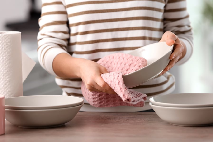 Pratos são enxugados com um pano de prato rosa.