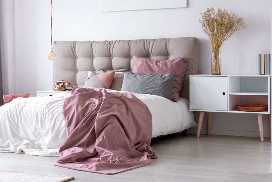 Cama de casal desarrumada com lencois rosa e branco caindo no chao